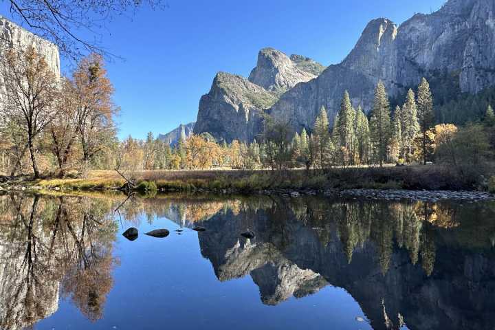Mountains and trees reflected in a calm lake under a clear blue sky.